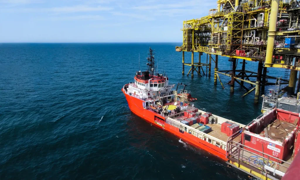 A Platform Supply Vessel approaching an offshore oil platform with cargo visible on deck